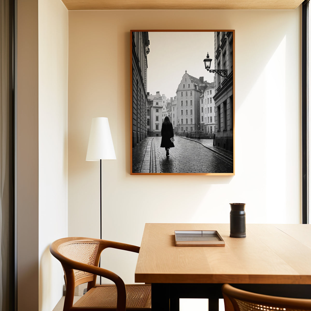 Woman walking on cobblestone old town street print in an oak frame above a dining table and cane chair