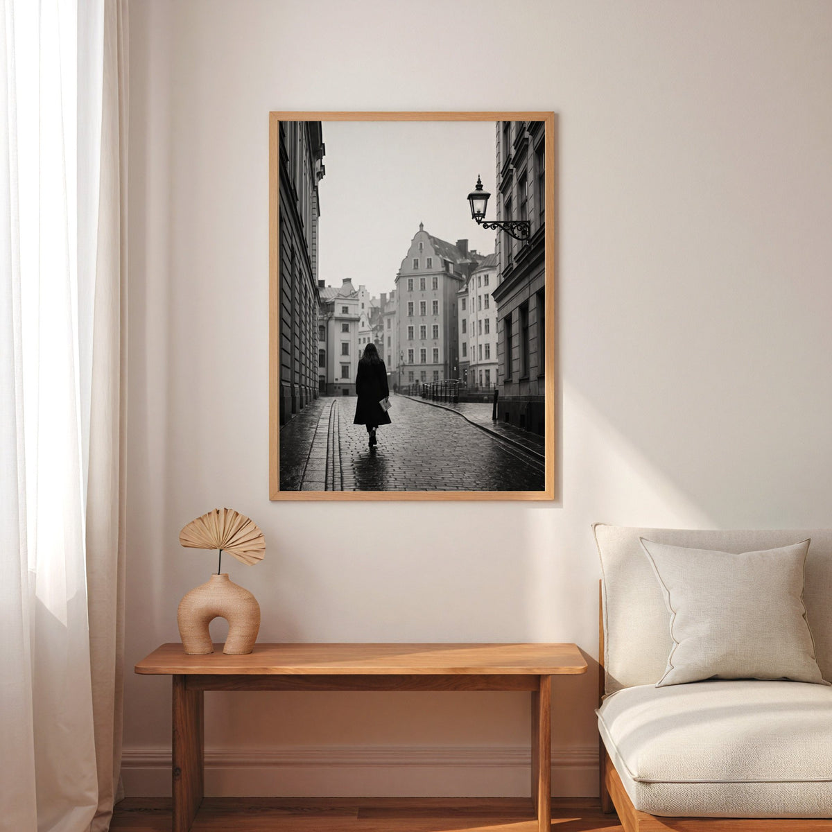 Woman walking on cobblestone old town street print in an oak frame above a narrow console with an arched vase