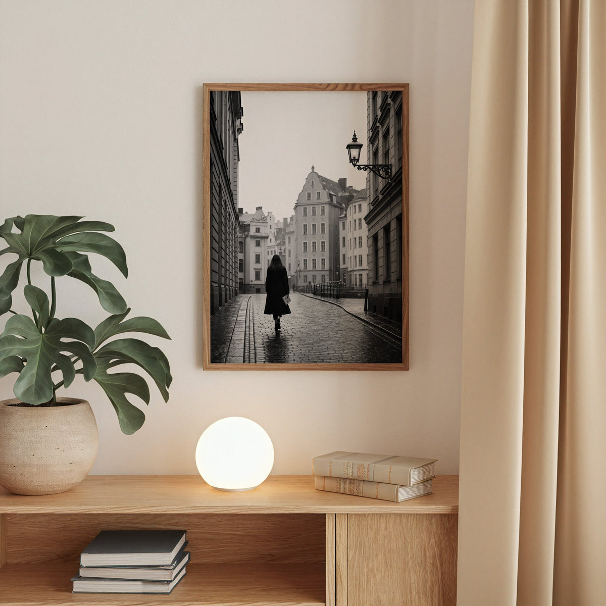Woman walking on cobblestone old town street print in a walnut frame above an oak cabinet with a glowing globe lamp