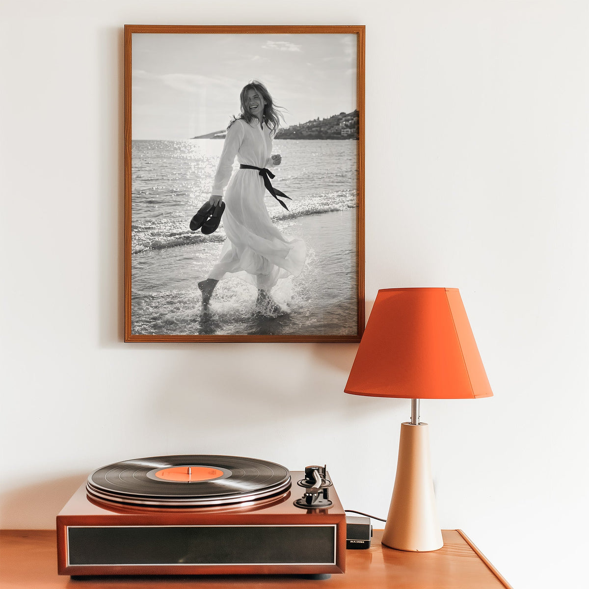 Laughing woman in white dress running in the surf print in a walnut frame above a record player and orange lamp