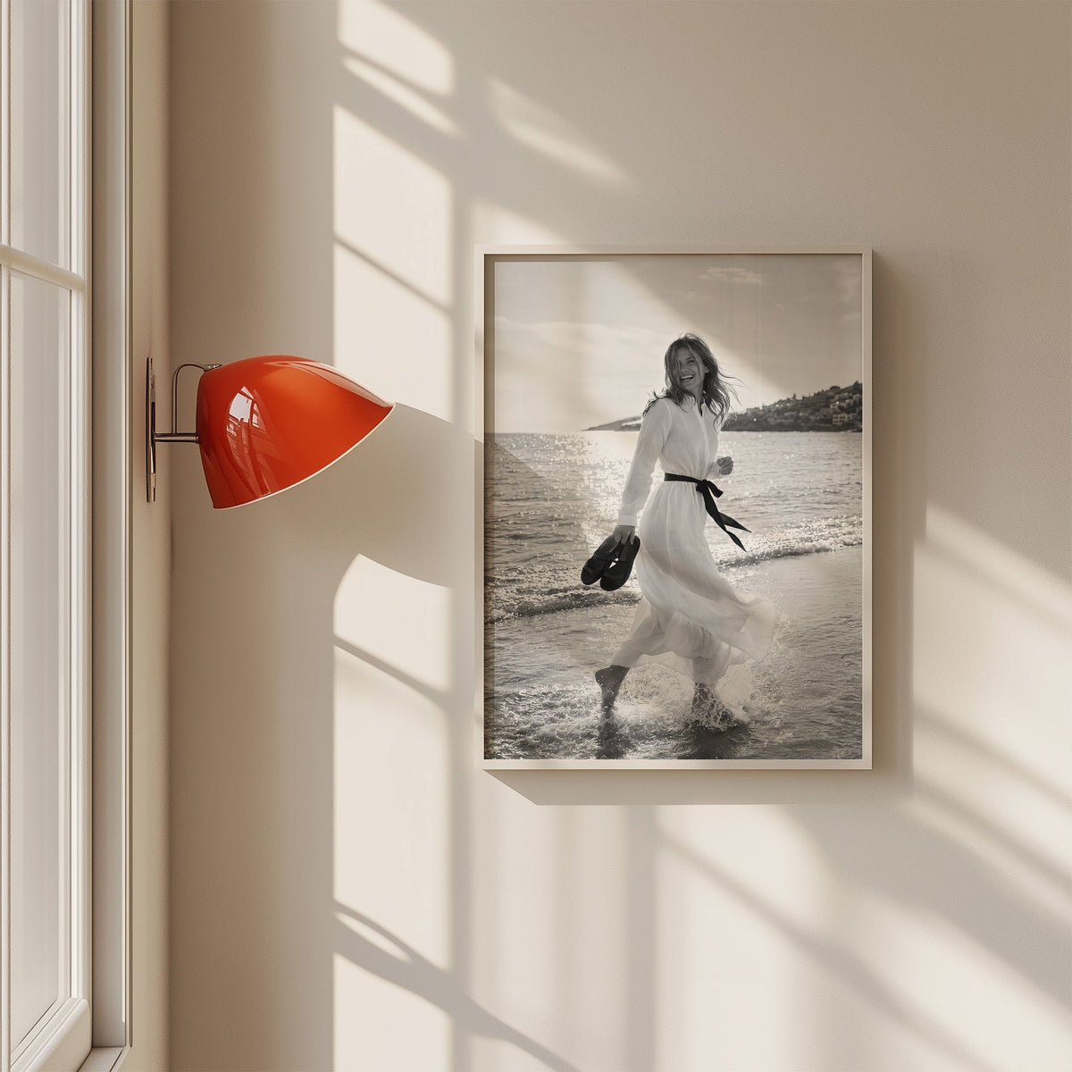 Laughing woman in white dress running in the surf print in a white frame on a sunlit wall beside a red sconce