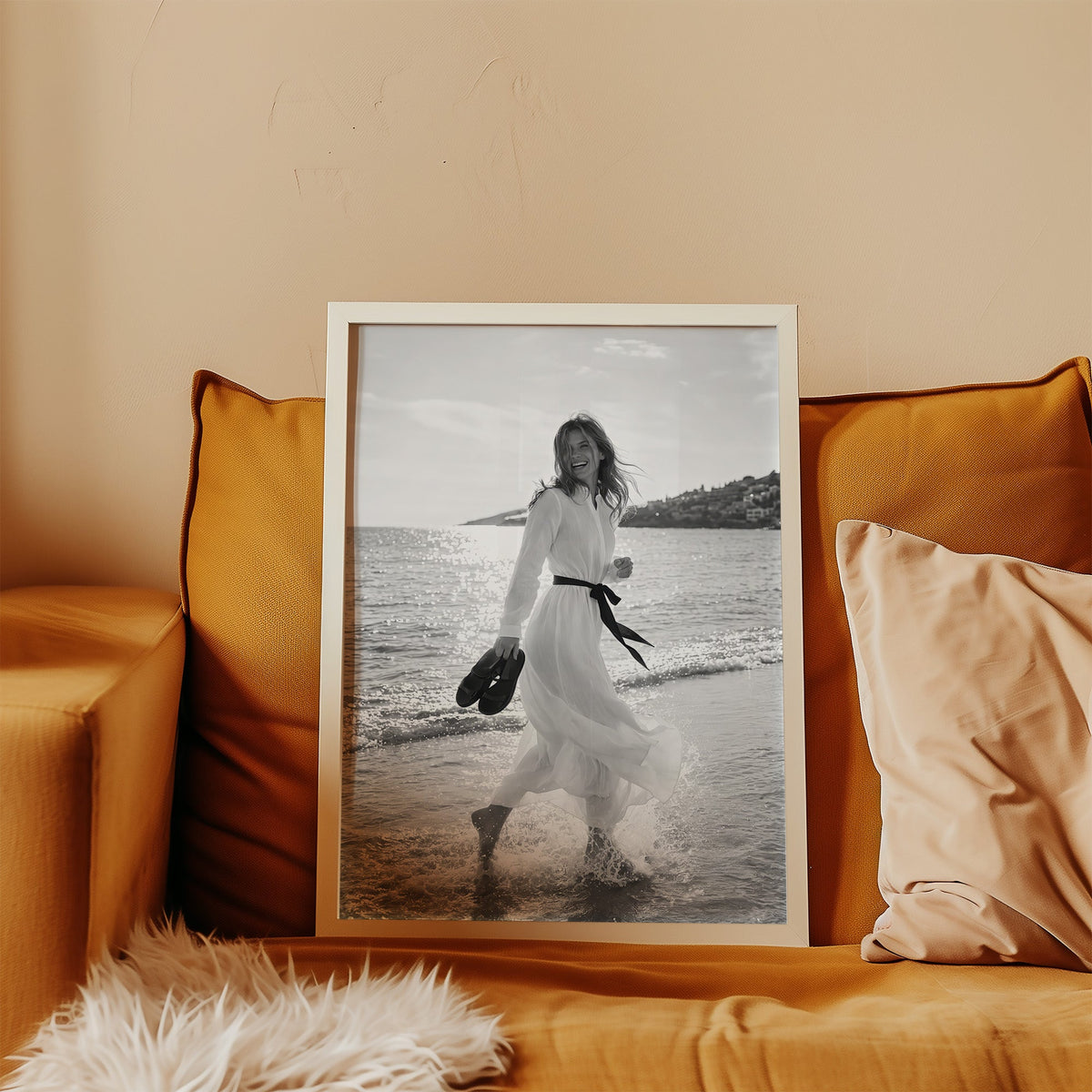 Laughing woman in white dress running in the surf print in a white frame leaning on a mustard velvet sofa