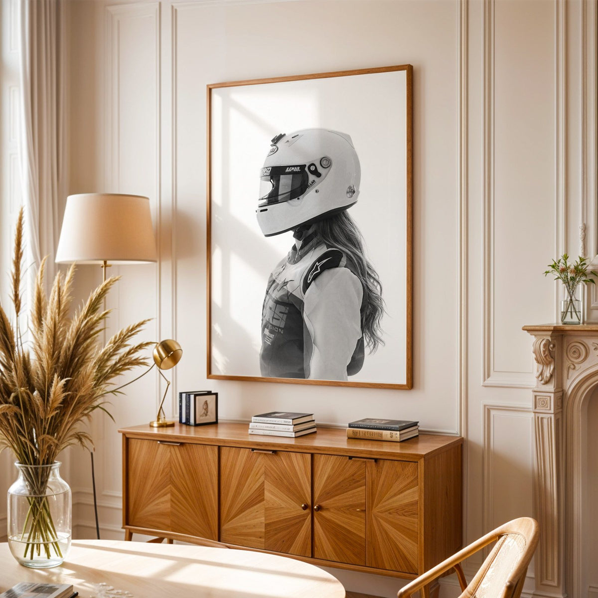 Woman in white racing helmet seen in profile print in an oak frame above a sunburst wood sideboard with pampas grass