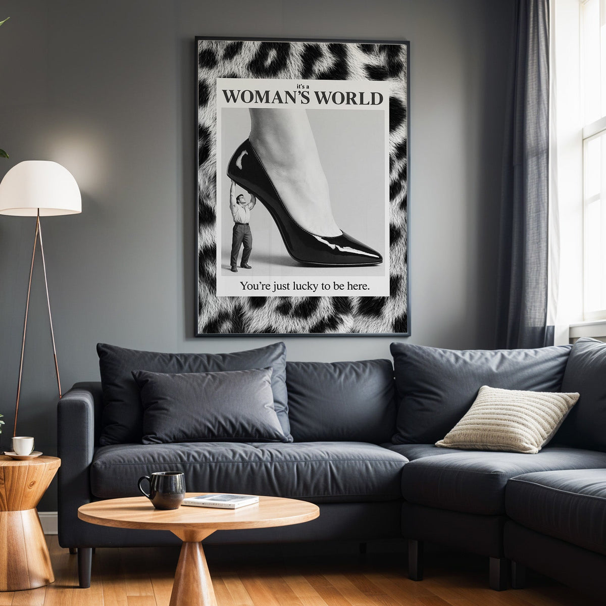 Tiny man lifting giant stiletto in leopard frame print in a black frame above a charcoal sofa on a grey wall