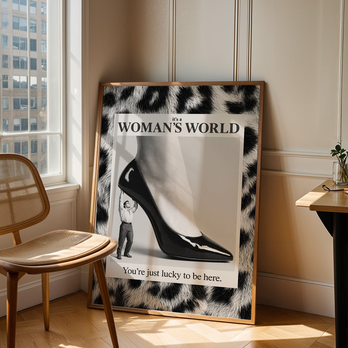 Tiny man lifting giant stiletto in leopard frame print in an oak frame leaning in a sunlit corner beside a cane chair