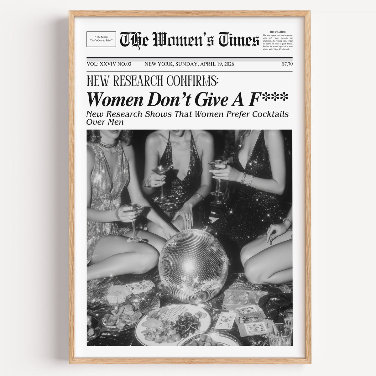Mock front page with women around a disco ball print in a light oak frame on a plain white wall