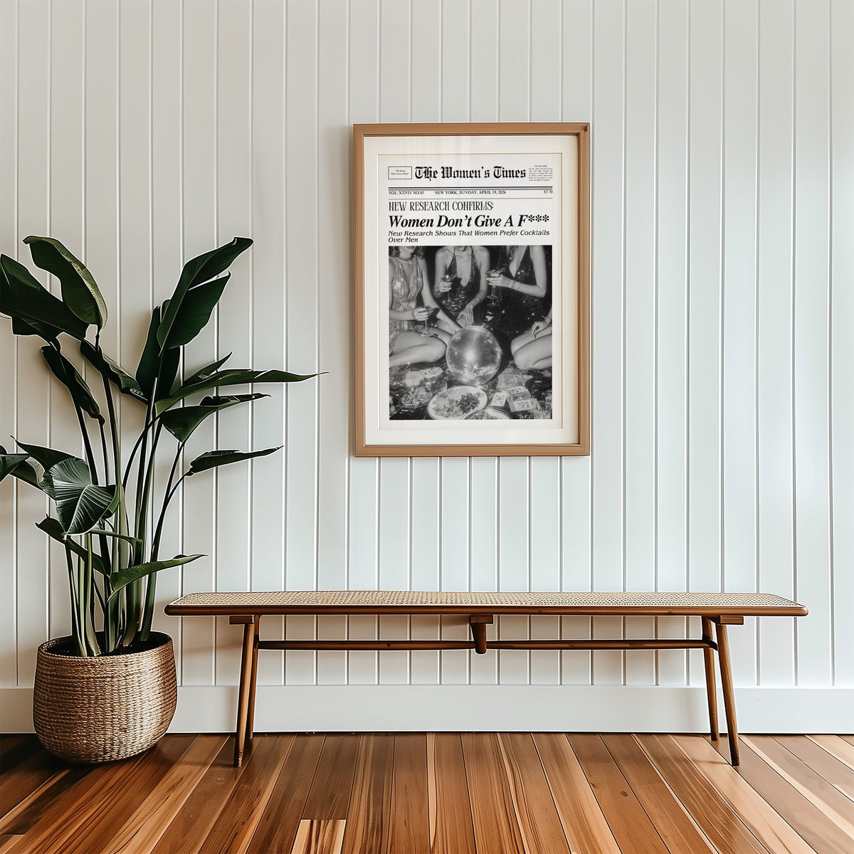 Mock front page with women around a disco ball print in a wood frame with a white mat above a cane bench
