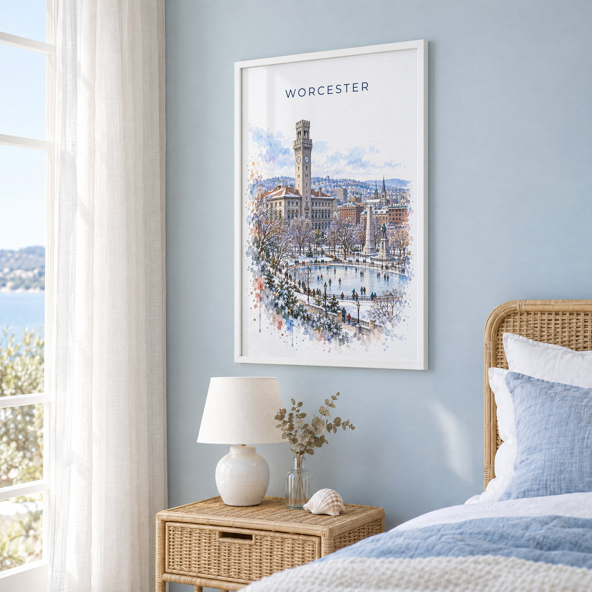 Worcester, Massachusetts watercolor print in a white frame on a pale blue wall beside a rattan bed in a coastal bedroom