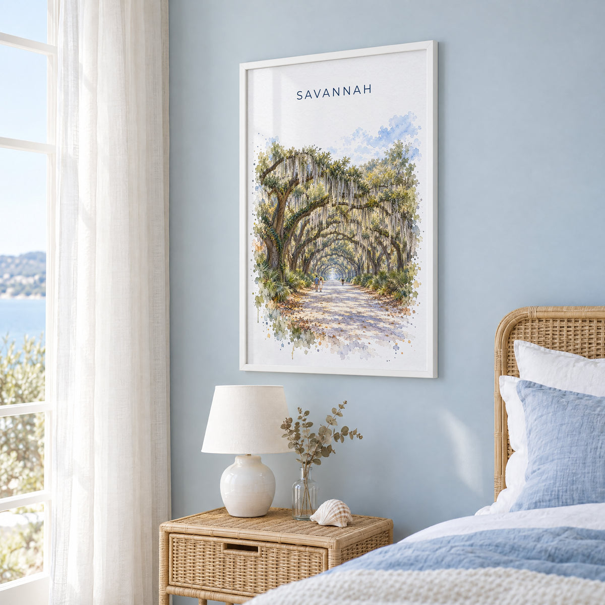 Wormsloe Savannah watercolor print in a white frame on a pale blue wall beside a rattan bed in a coastal bedroom