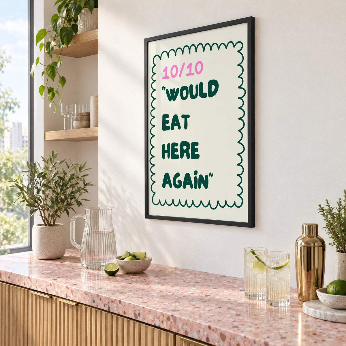 Would Eat Here Again 10/10 print in a black frame above a pink terrazzo cocktail counter with limes, seen at an angle