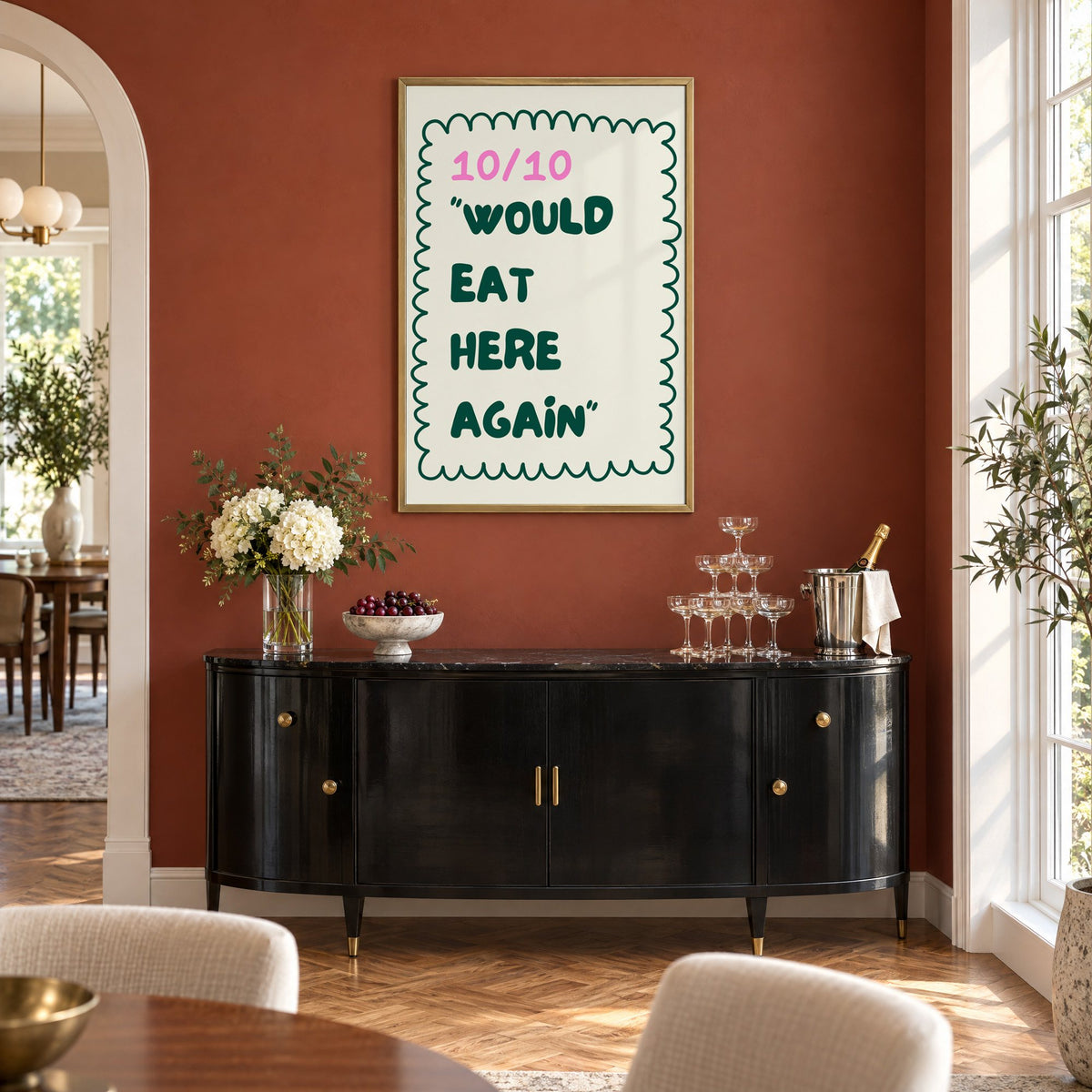 Would Eat Here Again 10/10 print in a brass frame on a terracotta wall above a black buffet with a champagne tower