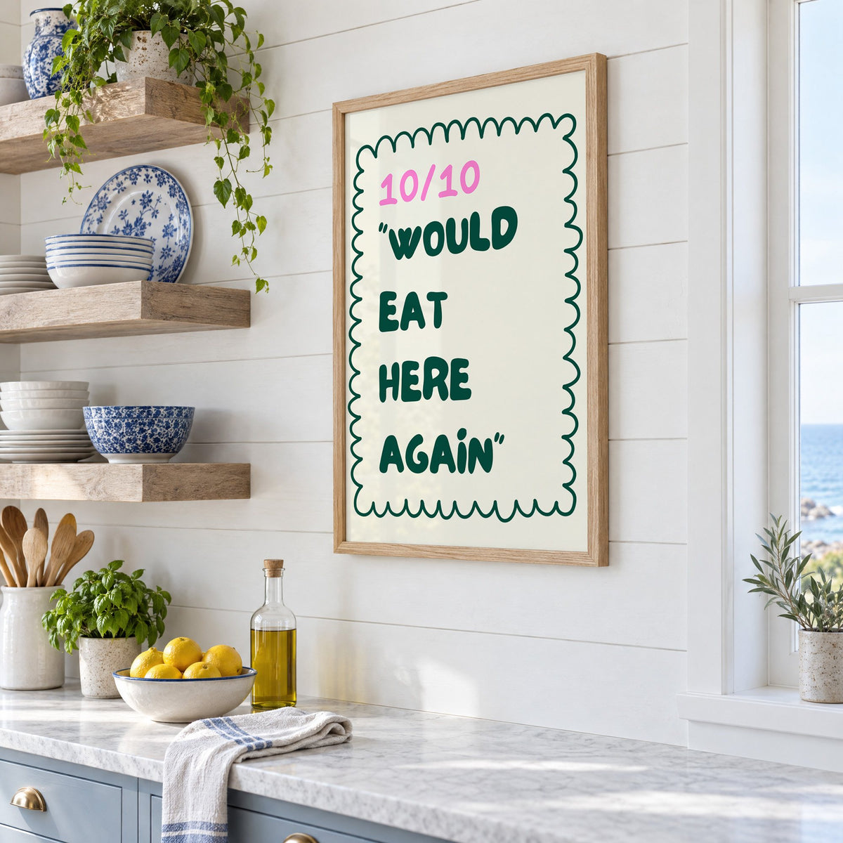 Would Eat Here Again 10/10 print in an oak frame in a white coastal kitchen beside blue and white plates