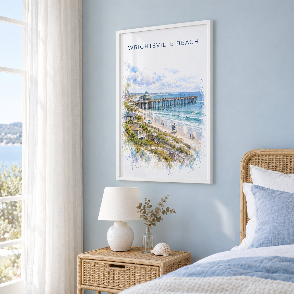 Wrightsville Beach watercolor print in a white frame on a pale blue wall beside a rattan bed in a coastal bedroom