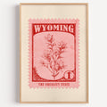 Wyoming state flower stamp print in red on pink, light oak frame on a plain white wall
