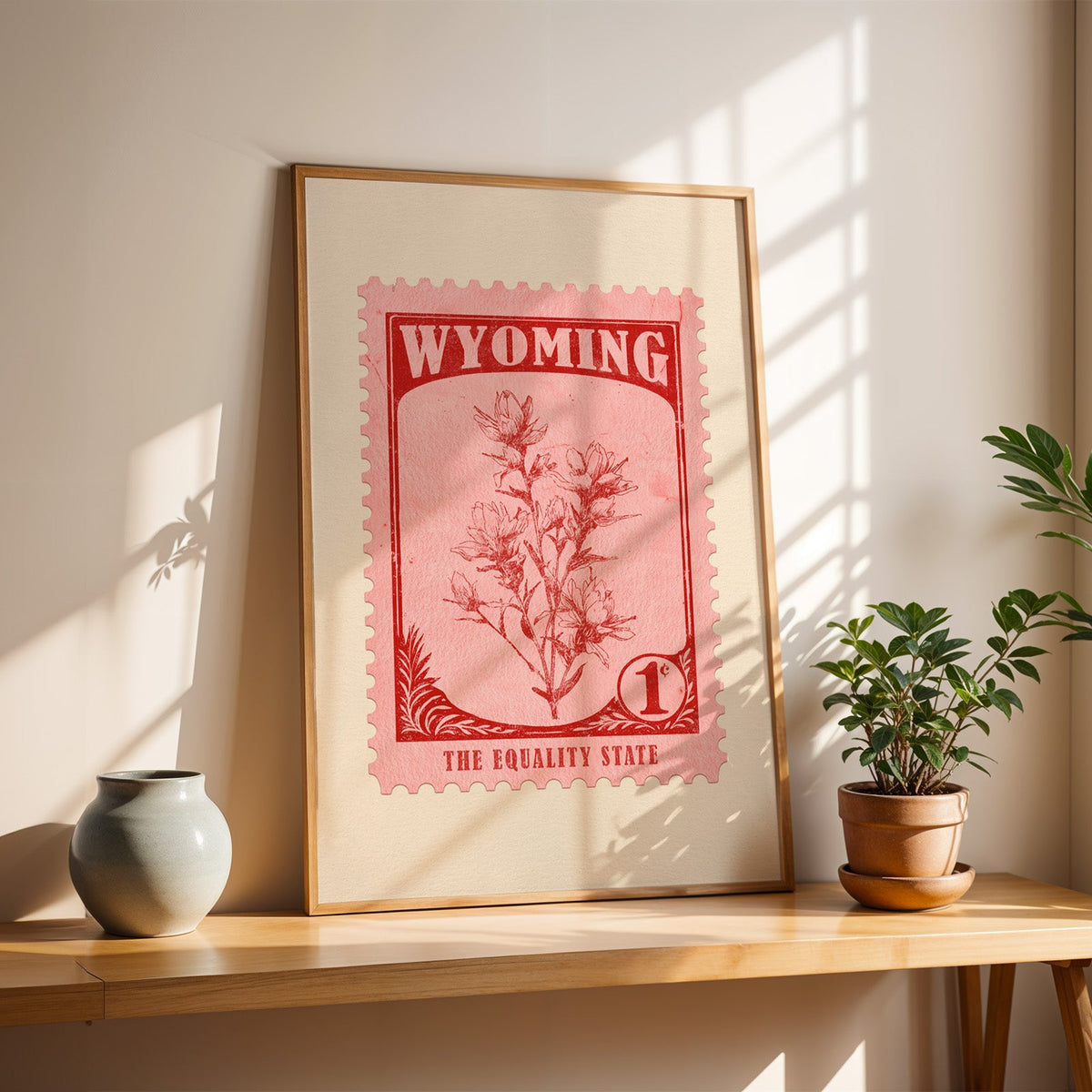Wyoming Indian Paintbrush stamp print in a light oak frame leaning on a table beside a stoneware vase