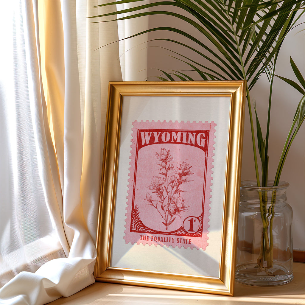 Wyoming stamp print in a gold frame leaning by a cream curtain with a palm in a glass jar