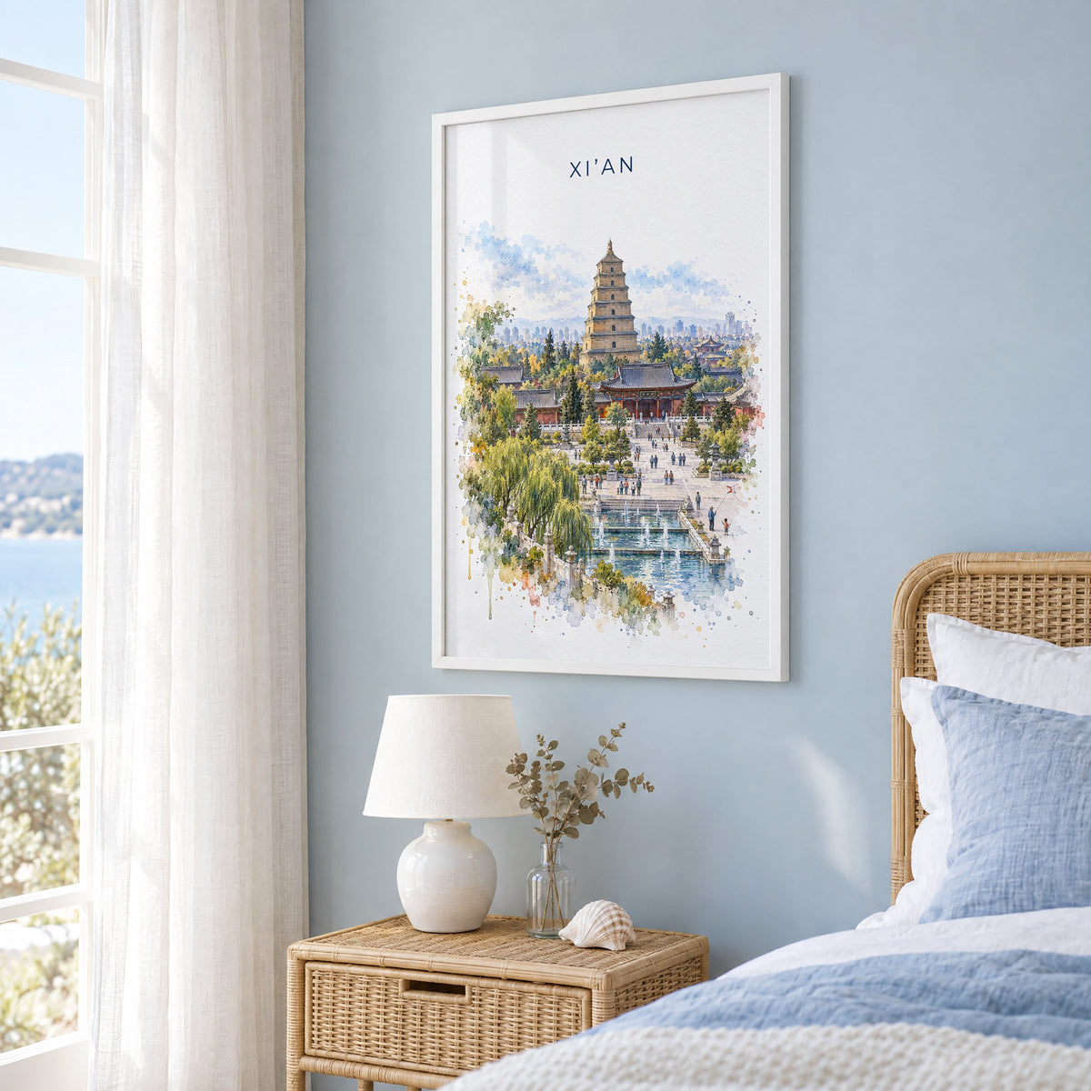 Xi'an watercolor print in a white frame on a pale blue wall beside a rattan bed in a coastal bedroom