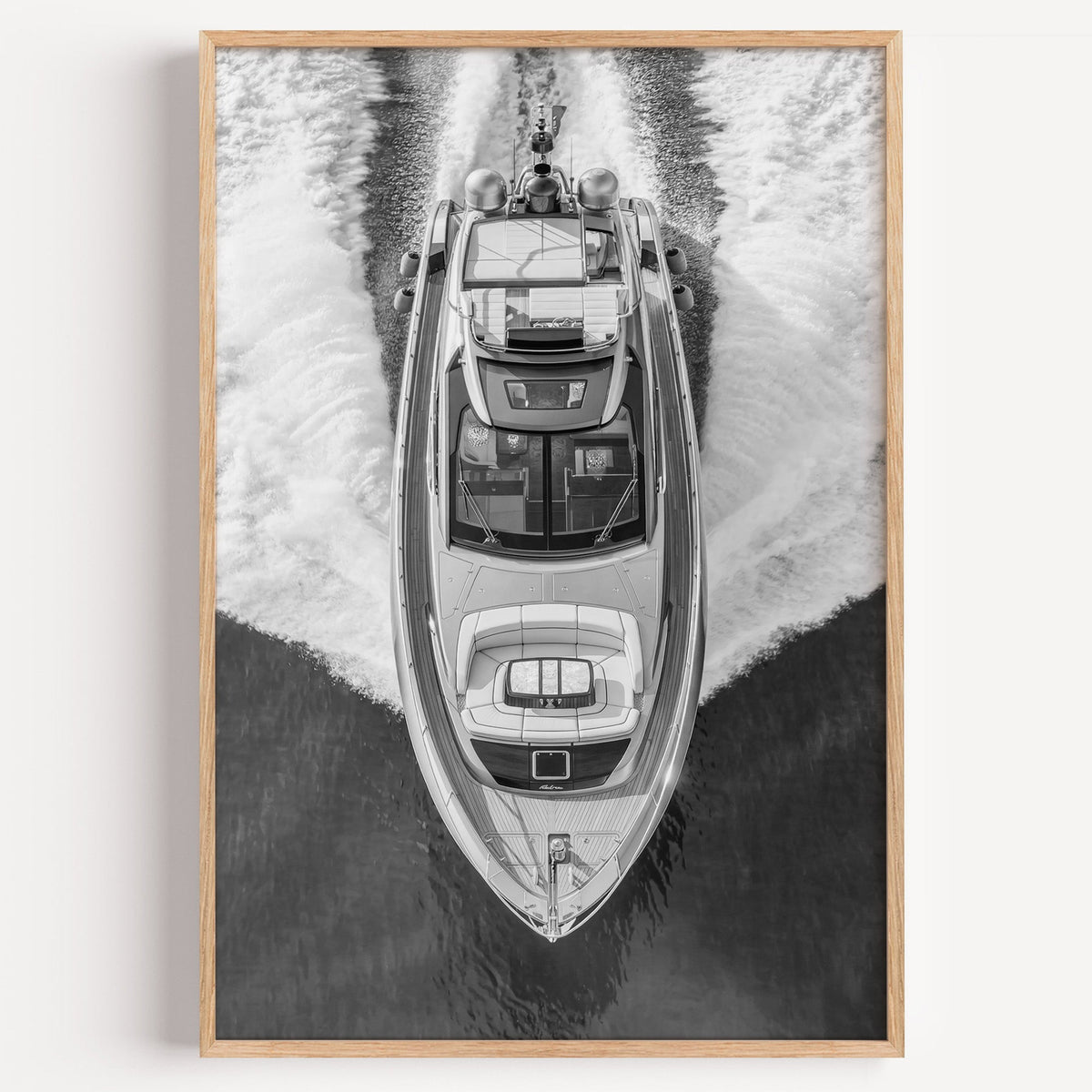 Aerial view of a yacht with white wake print in a light oak frame on a plain white wall