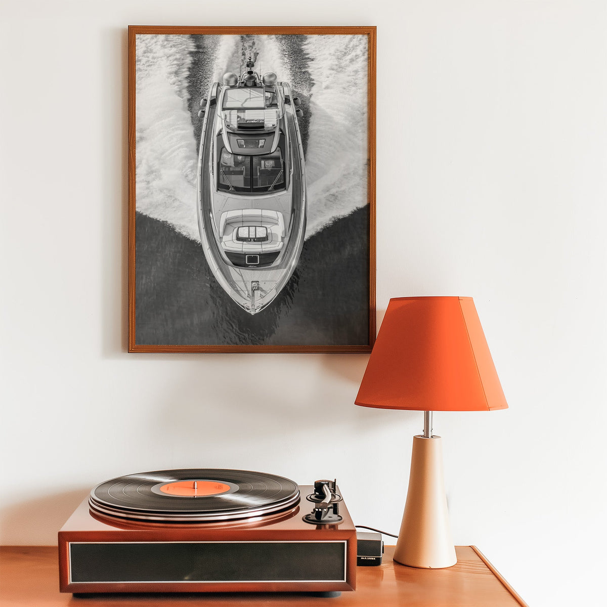 Aerial view of a yacht with white wake print in a walnut frame above a record player and orange lamp