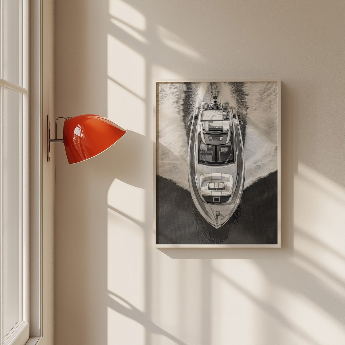Aerial view of a yacht with white wake print in a white frame on a sunlit wall beside a red sconce