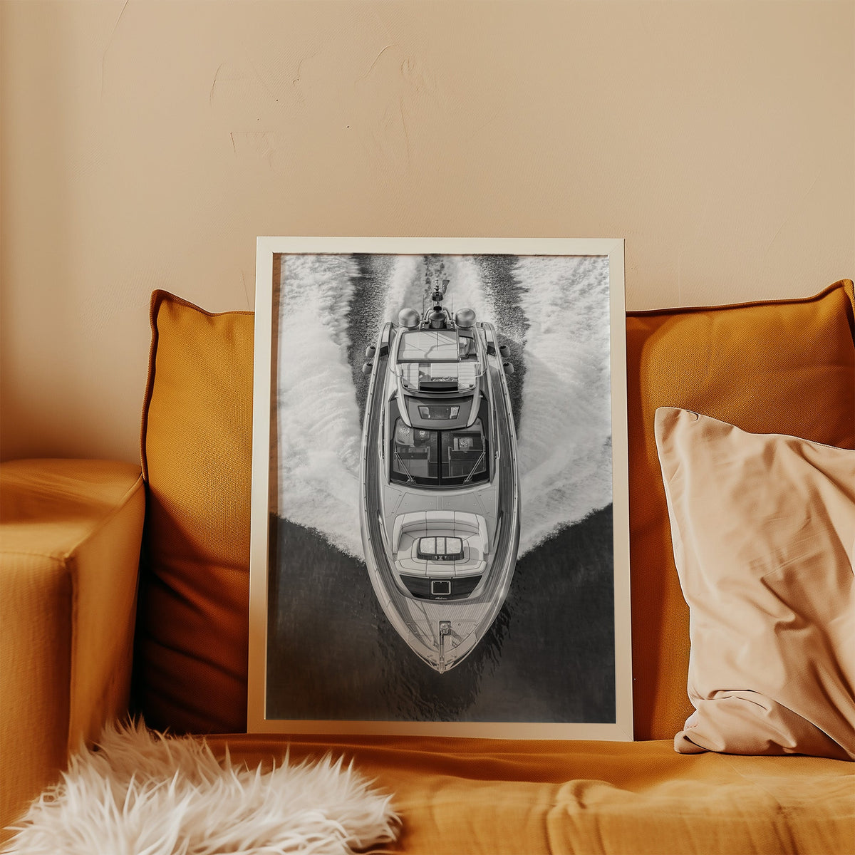 Aerial view of a yacht with white wake print in a white frame leaning on a mustard velvet sofa