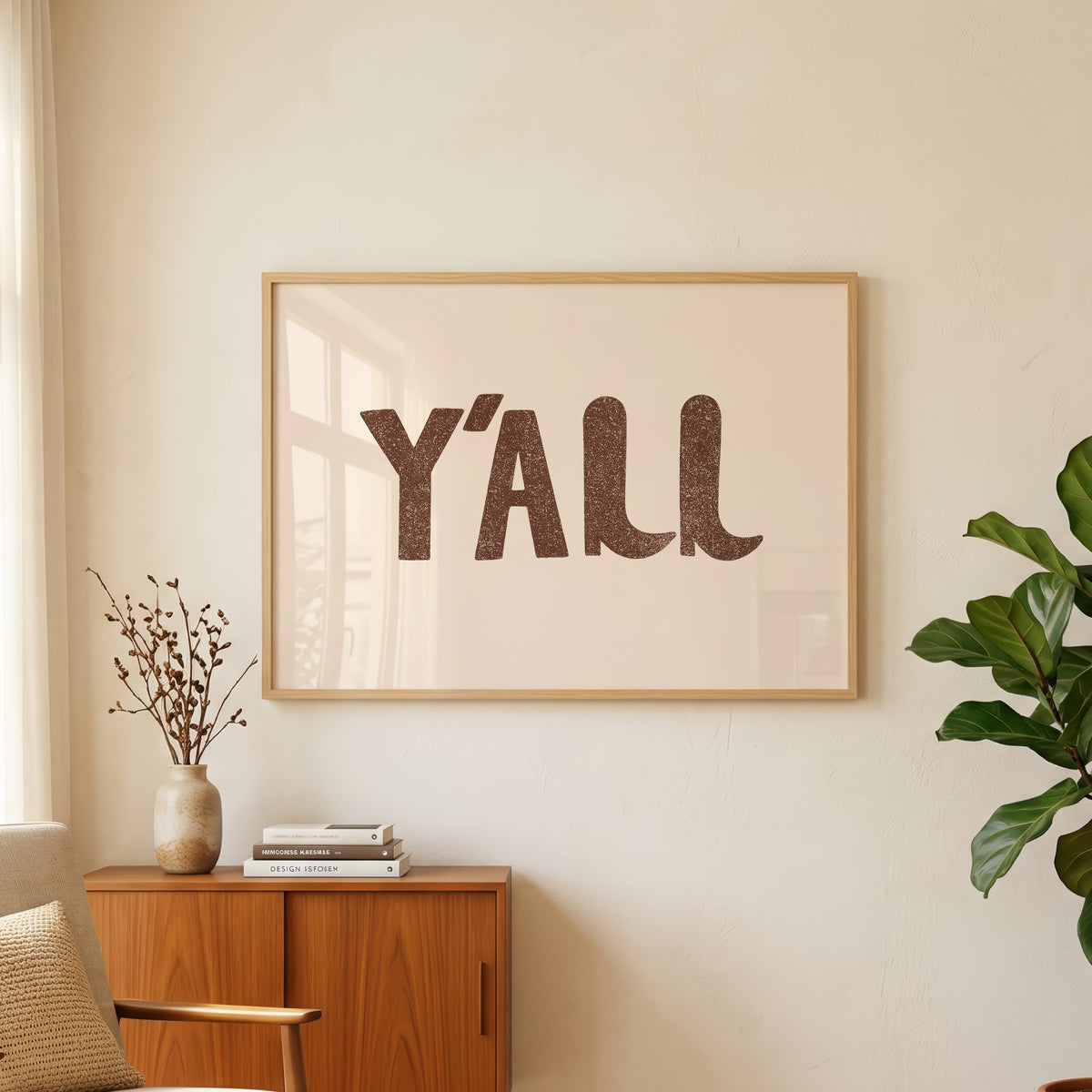 Y'all bold type cream print in an oak frame above a teak sideboard with a fig plant
