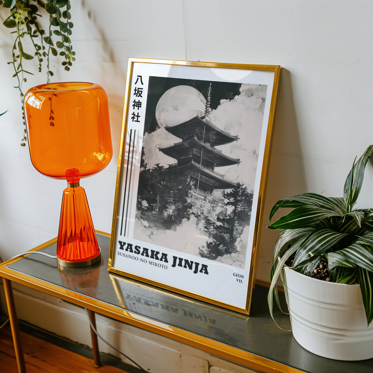 Sumi-e Yasaka pagoda and full moon print shown in a gold frame on a console beside an orange glass lamp
