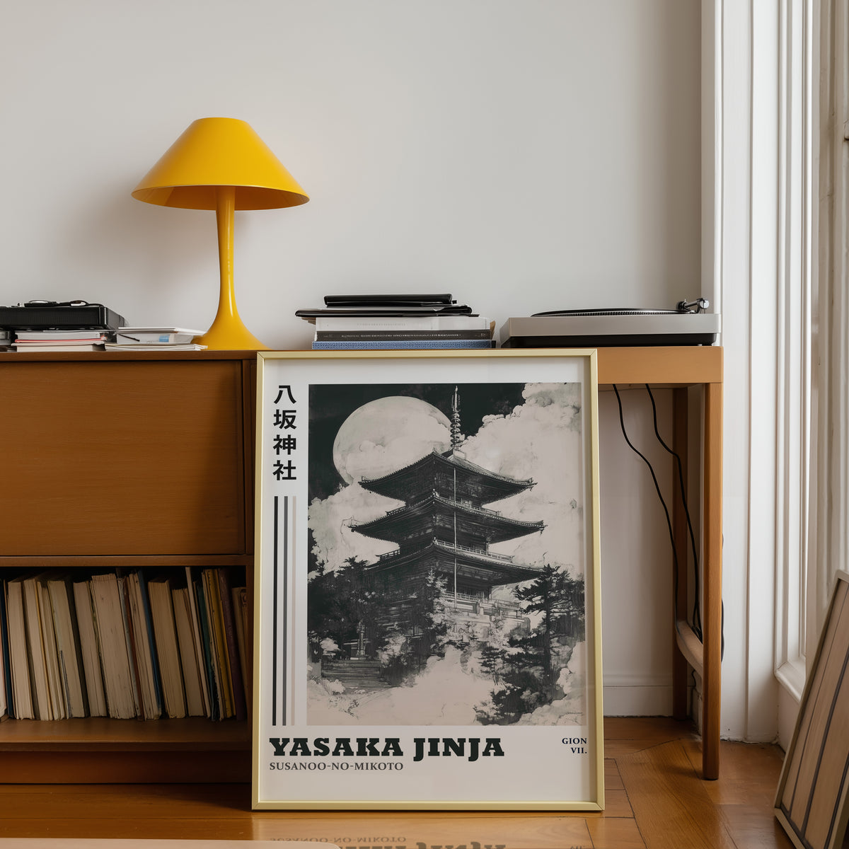 Sumi-e Yasaka pagoda and full moon print shown in a gold frame below a teak desk with a yellow lamp