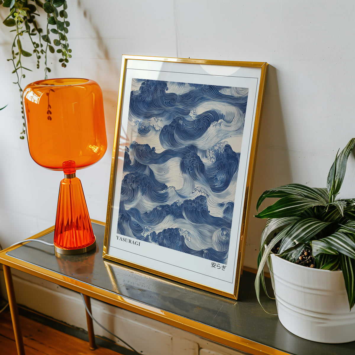 Indigo woodblock Yasuragi waves print shown in a gold frame on a console beside an orange glass lamp