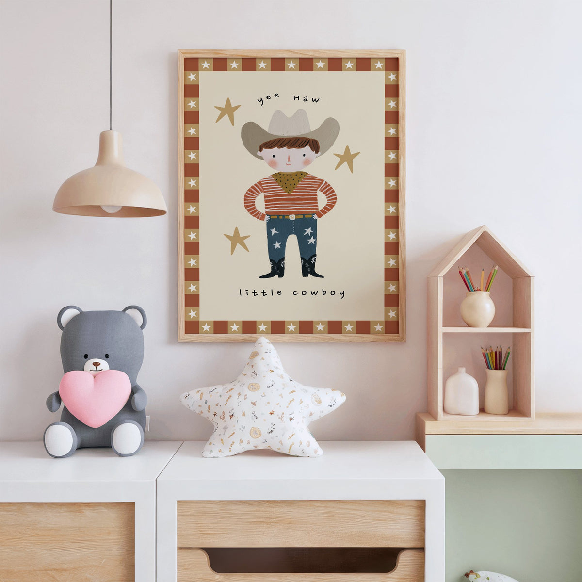 Yee haw cowboy star border nursery print in an oak frame above a white dresser with a star pillow and house shelf
