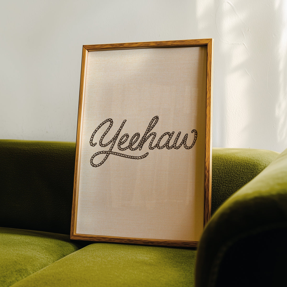 Yeehaw rope script print in an oak frame leaning on a green velvet sofa