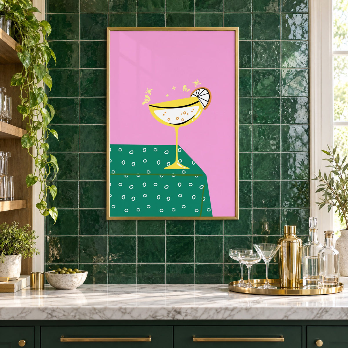 Yellow coupe cocktail print in a brass frame on emerald green tiles above a home bar with coupe glasses