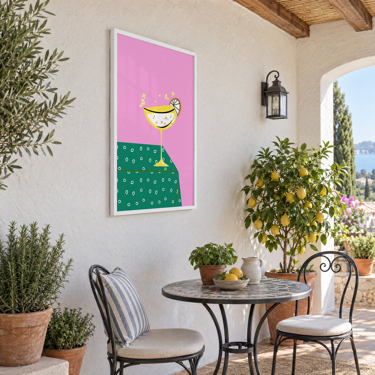 Yellow coupe cocktail print in a white frame on a sunny patio wall beside a potted lemon tree