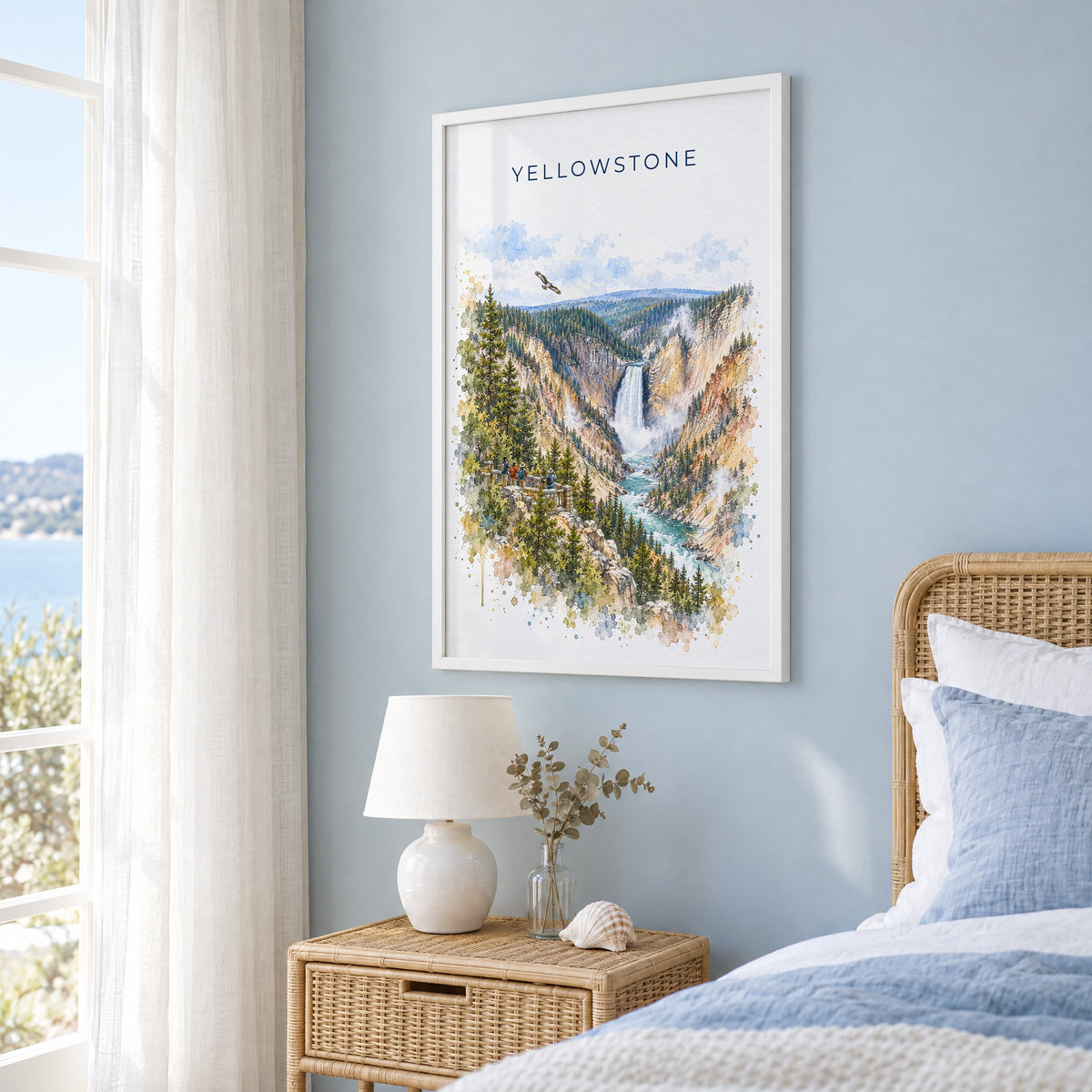 Yellowstone National Park watercolor print in a white frame on a pale blue wall beside a rattan bed in a coastal bedroom