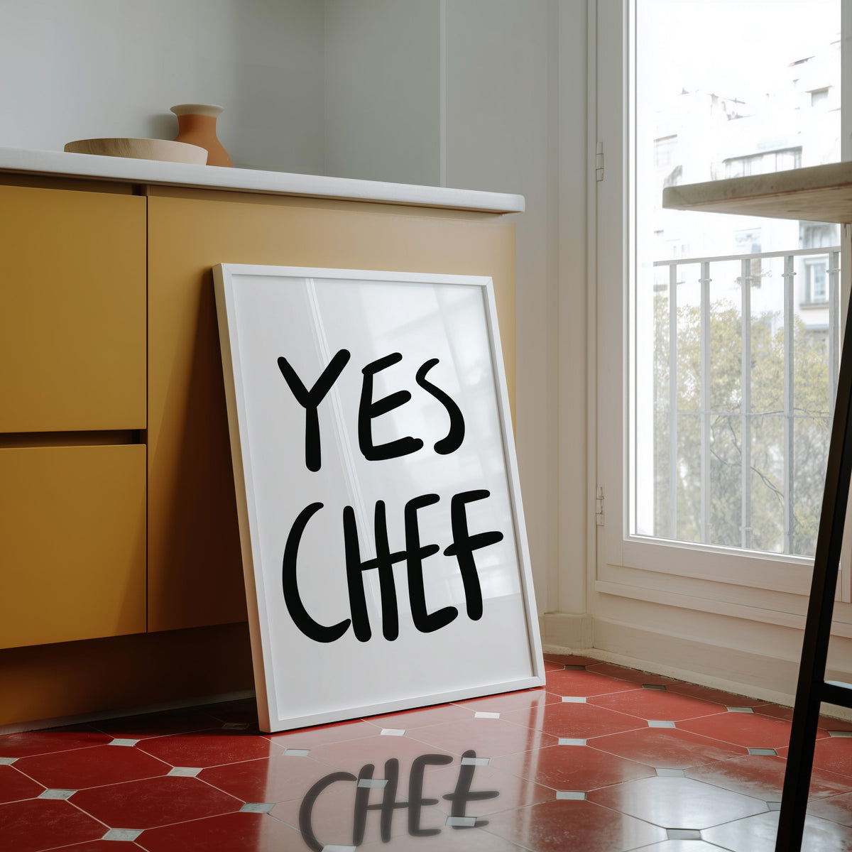 Yes Chef print in a white frame against yellow cabinets on a red tiled floor
