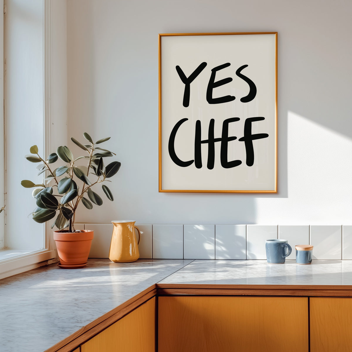 Yes Chef print in a gold frame above a marble counter with a yellow ceramic jug