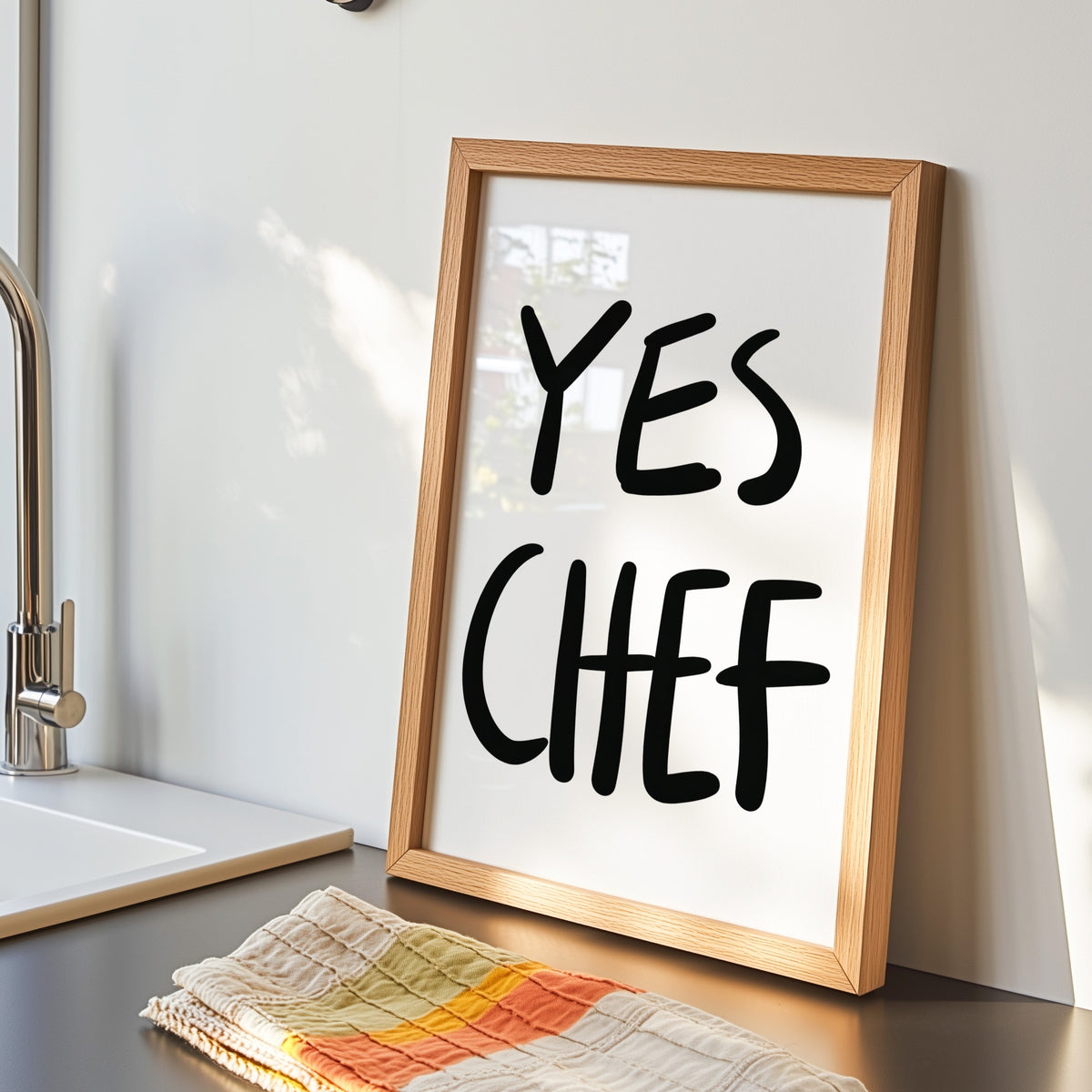 Yes Chef print in an oak frame by the kitchen sink beside a striped tea towel