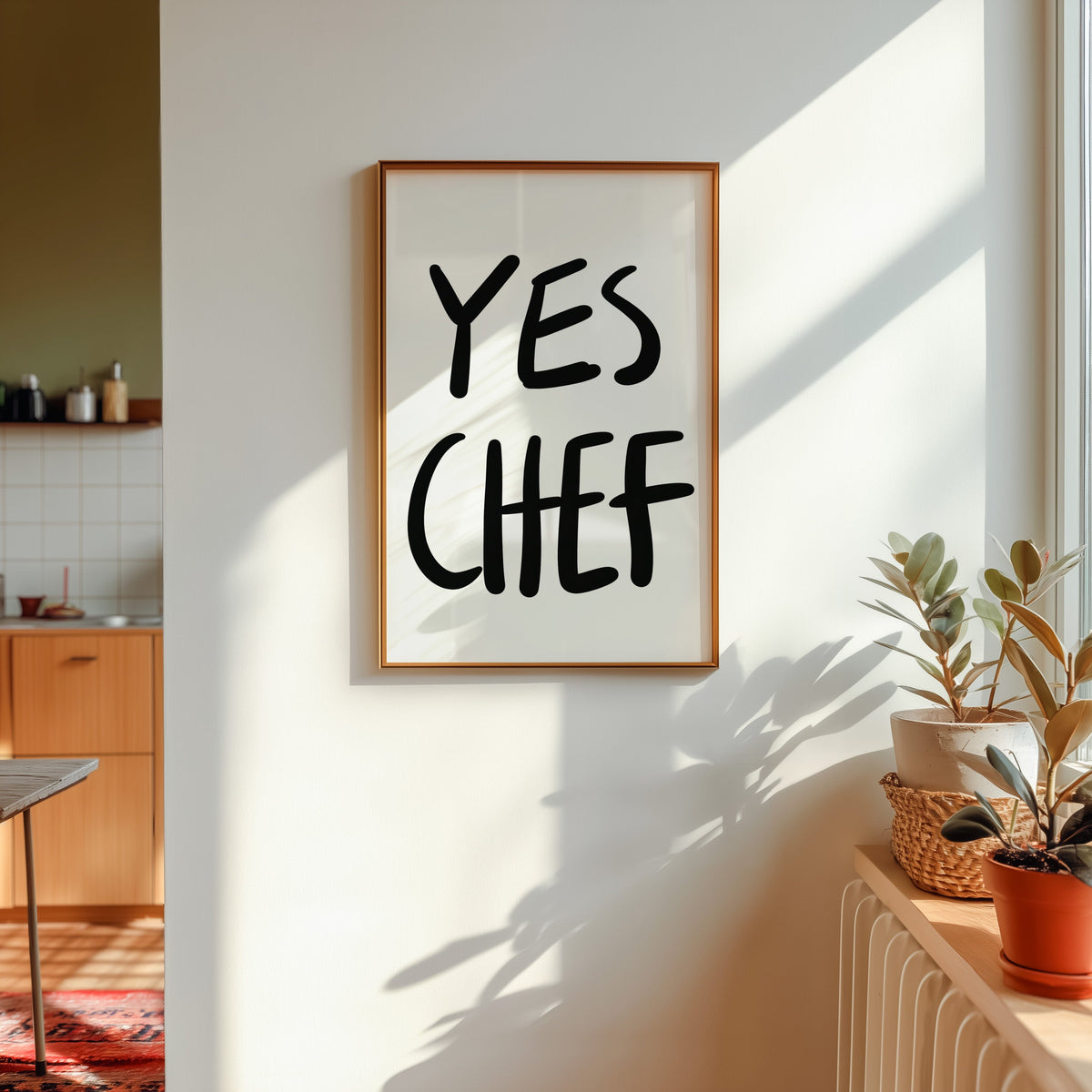 Yes Chef print in a gold frame in sunlight with plants and a kitchen beyond