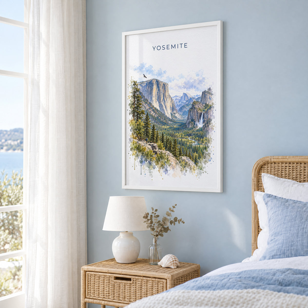 Yosemite National Park watercolor print in a white frame on a pale blue wall beside a rattan bed in a coastal bedroom