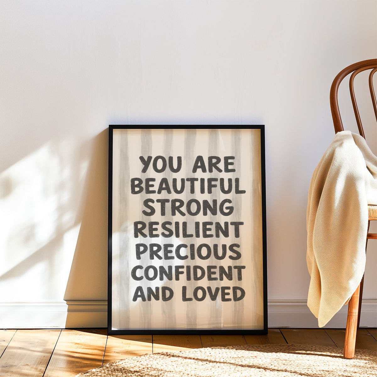You are beautiful affirmation quote print in a black frame leaning on a wood floor beside a bentwood chair