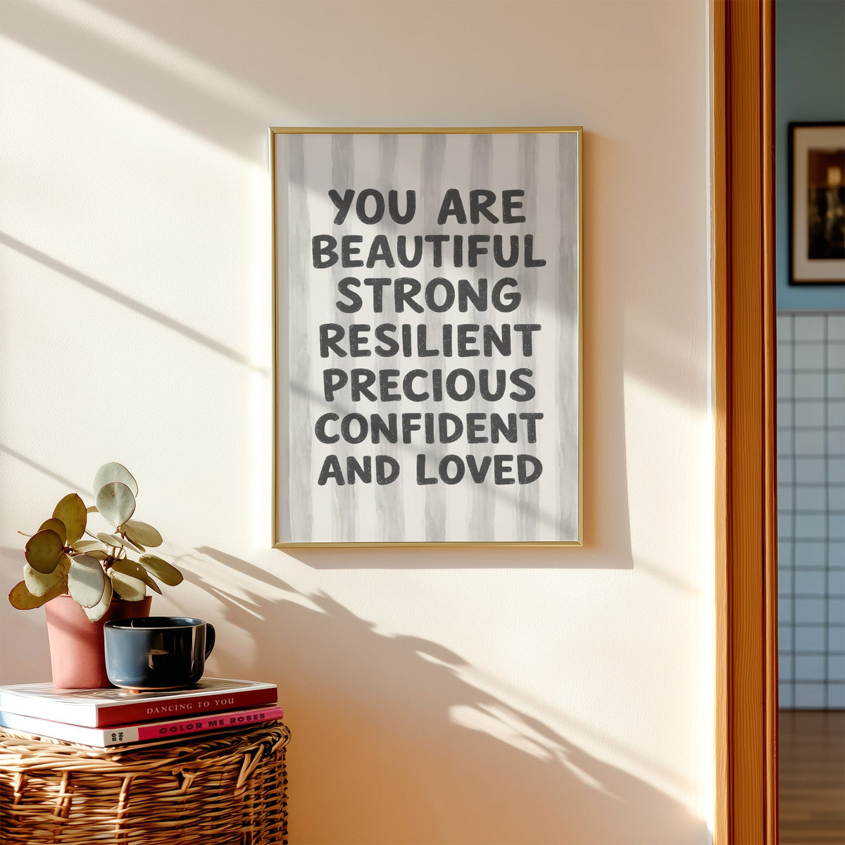 You are beautiful affirmation quote print shown in a gold frame above a wicker basket and stacked books