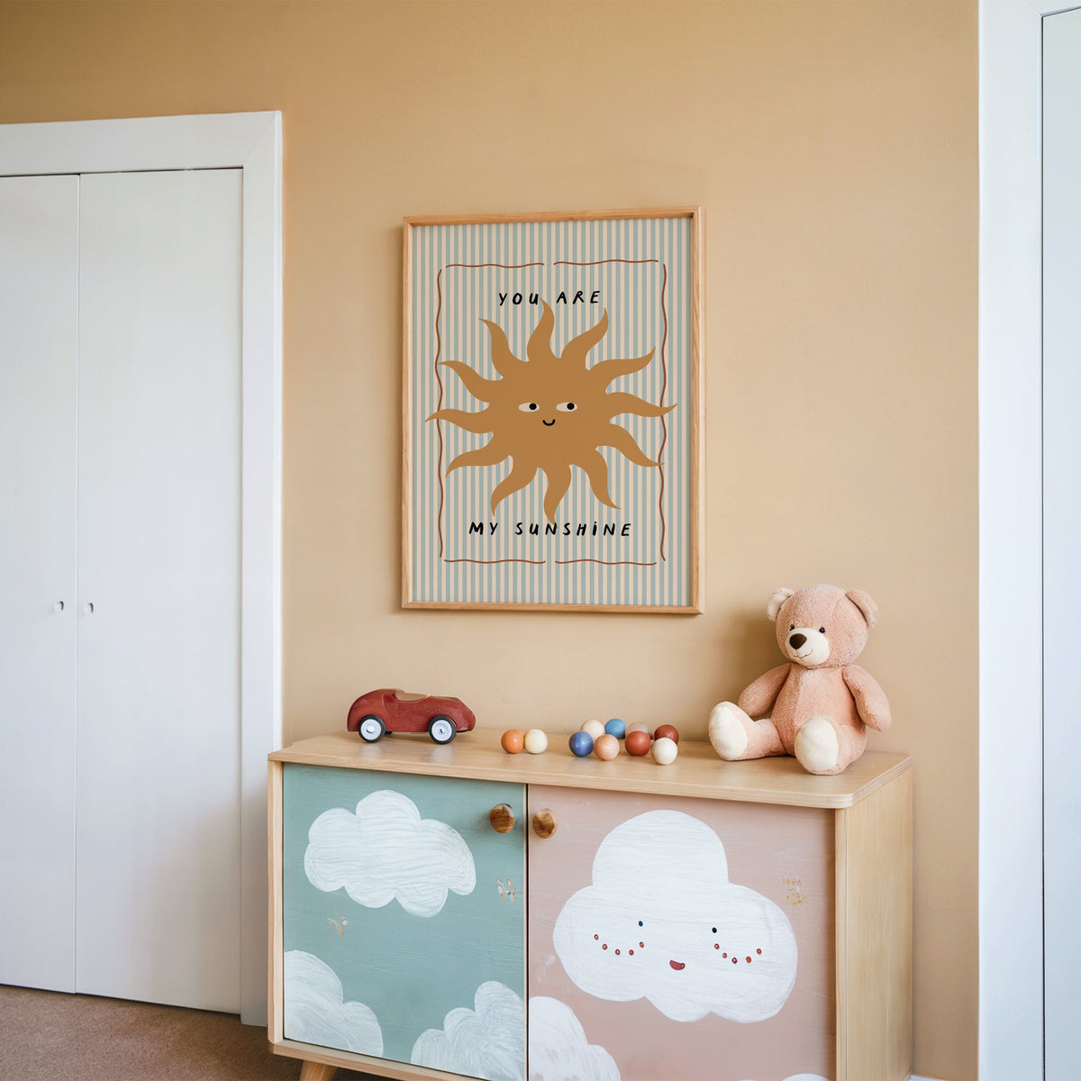 You are my sunshine sun nursery print in an oak frame on a peach wall above a cloud-painted cabinet