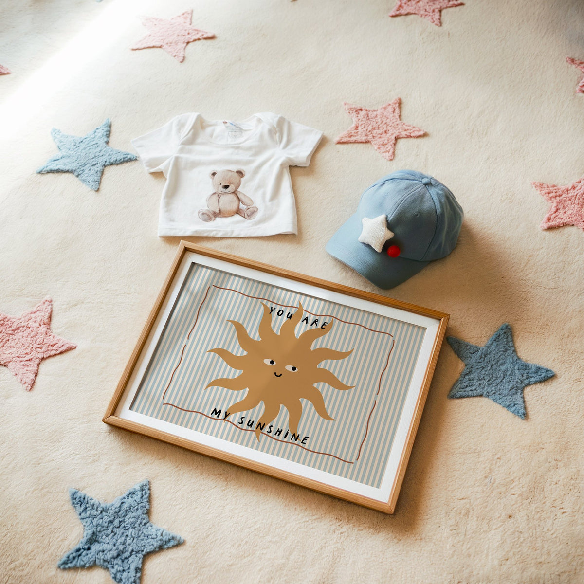 Landscape you are my sunshine sun nursery print in a matted oak frame on a star rug with a baby tee