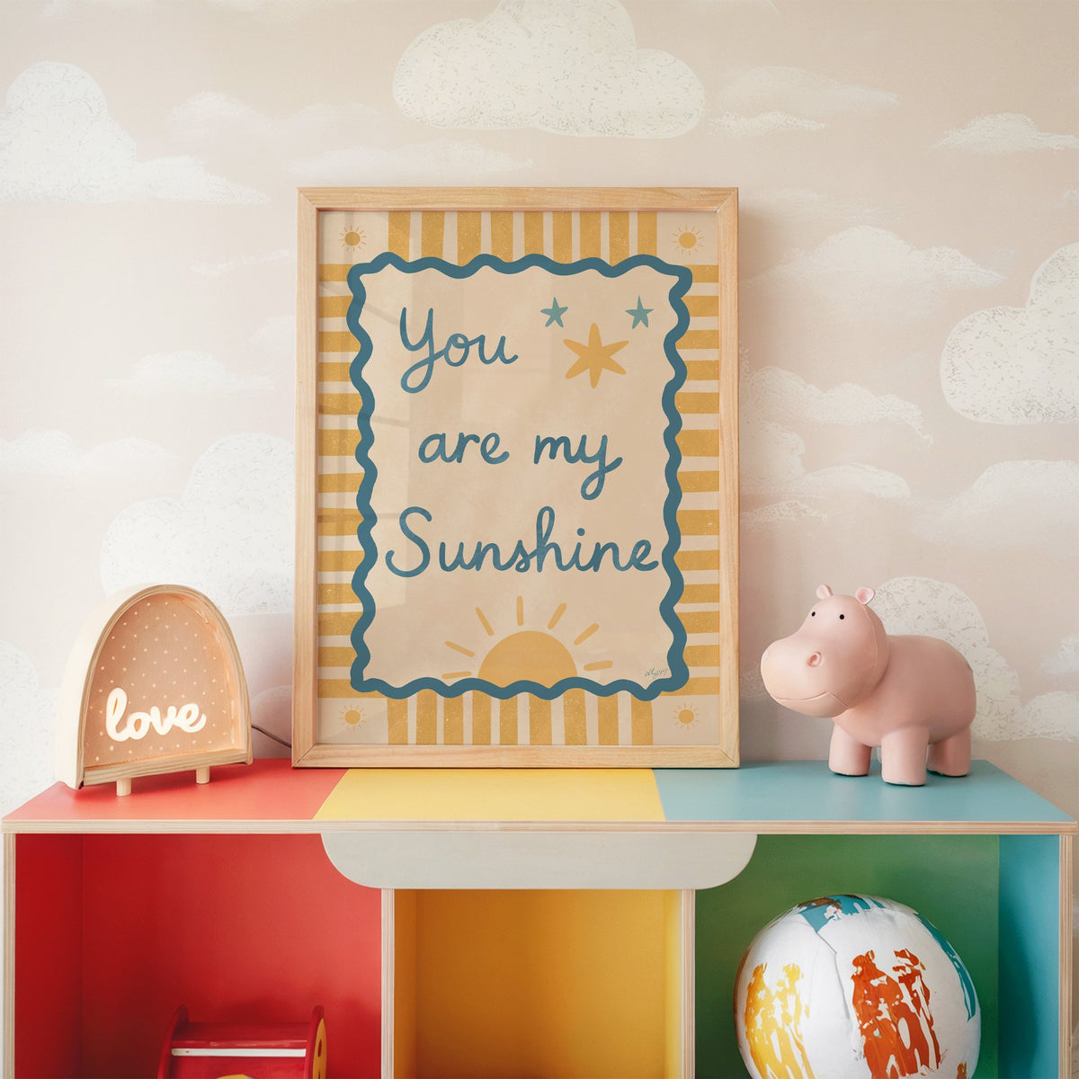 You are my sunshine wavy frame nursery print in an oak frame on a rainbow toy shelf against cloud wallpaper