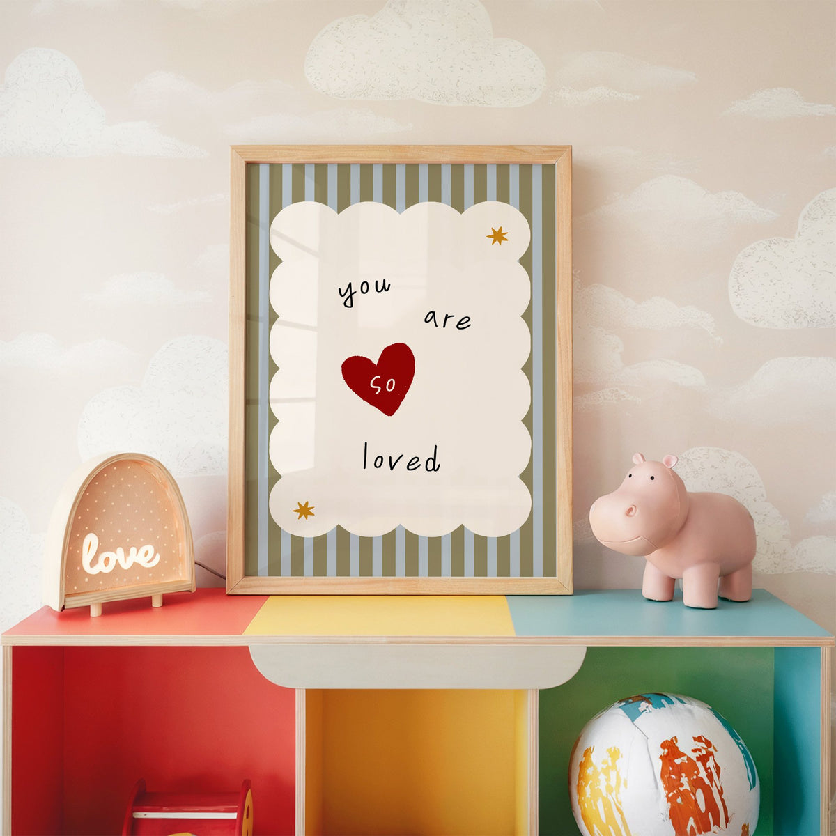 You are so loved heart nursery print in an oak frame on a rainbow toy shelf against cloud wallpaper