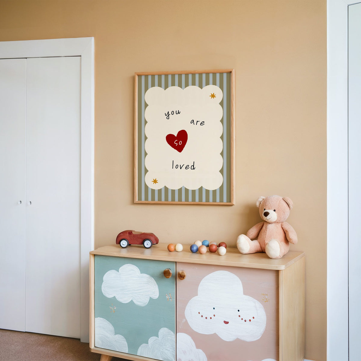 You are so loved heart nursery print in an oak frame on a peach wall above a cloud-painted cabinet