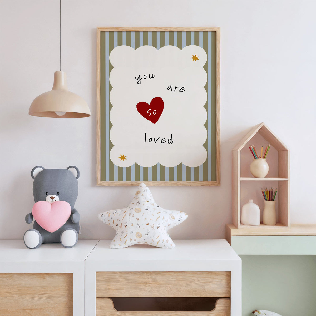 You are so loved heart nursery print in an oak frame above a white dresser with a star pillow and house shelf