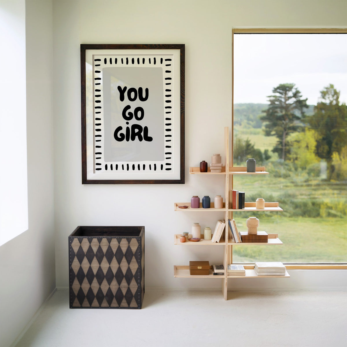 You go girl bubble letter quote print in a walnut frame with a white mat beside wooden shelves and a garden window
