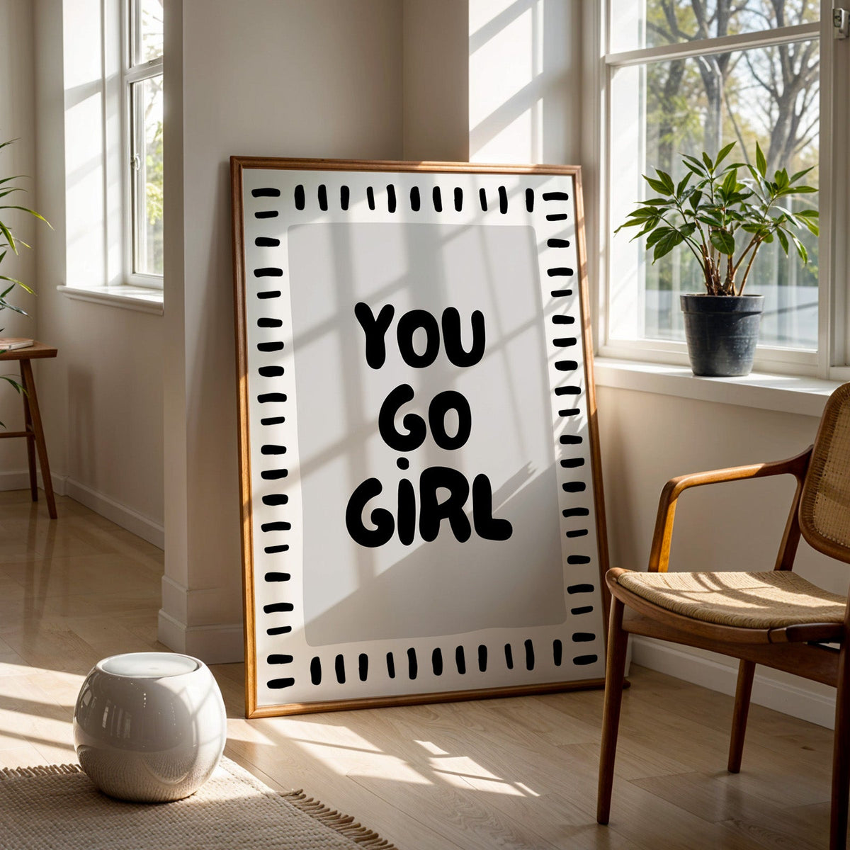 You go girl bubble letter quote print in a walnut frame on a wood floor beside a cane chair and sunny window