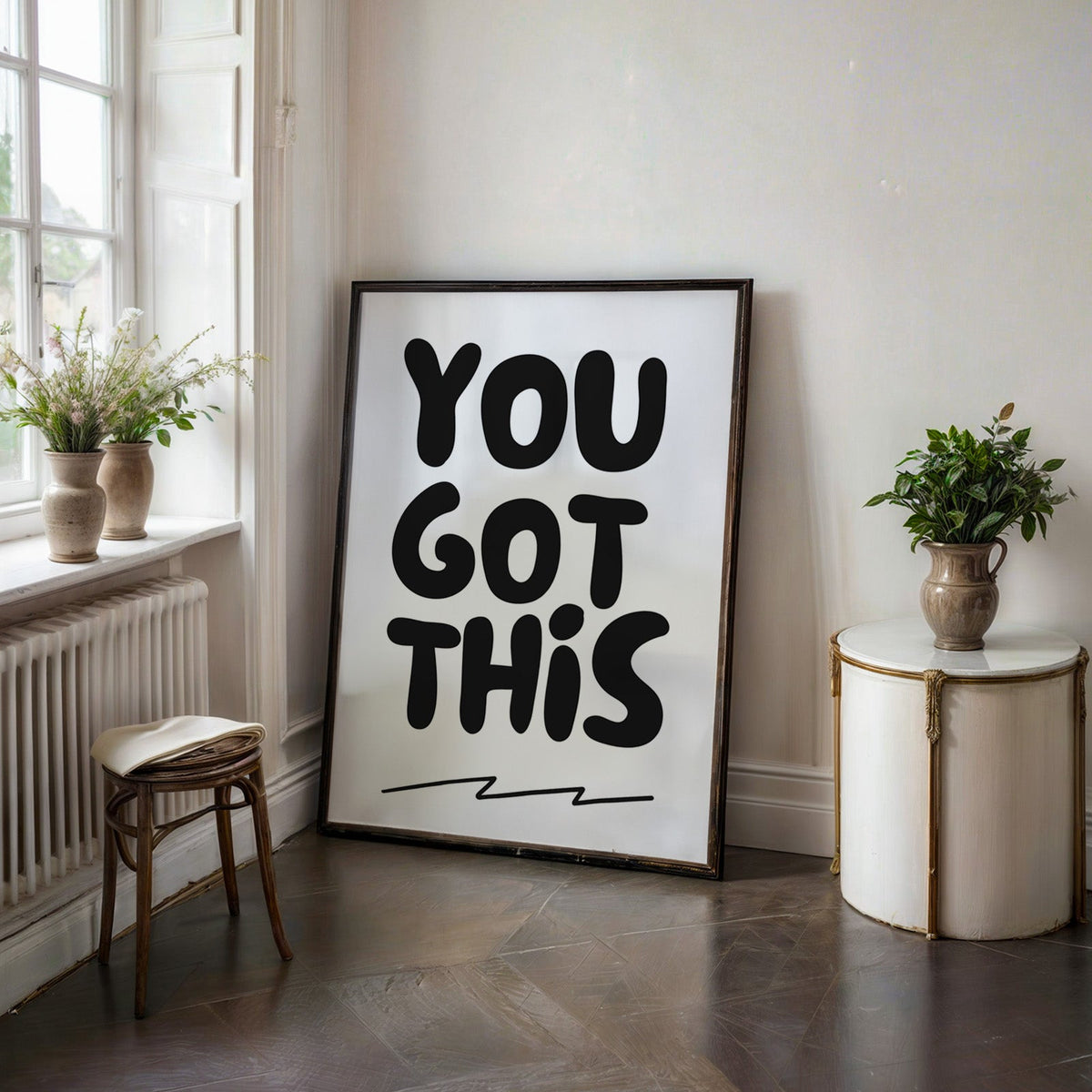 You got this bubble letter quote print in a black frame on a dark stone floor beside a white side table
